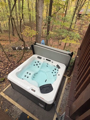 Un jacuzzi portatif installé dans un espace boisé, avec une terrasse en bois et des chaises à proximité.