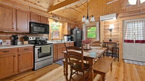 Interior de una cabaña de madera con cocina que cuenta con estufa, microondas, refrigerador y armarios de madera.
