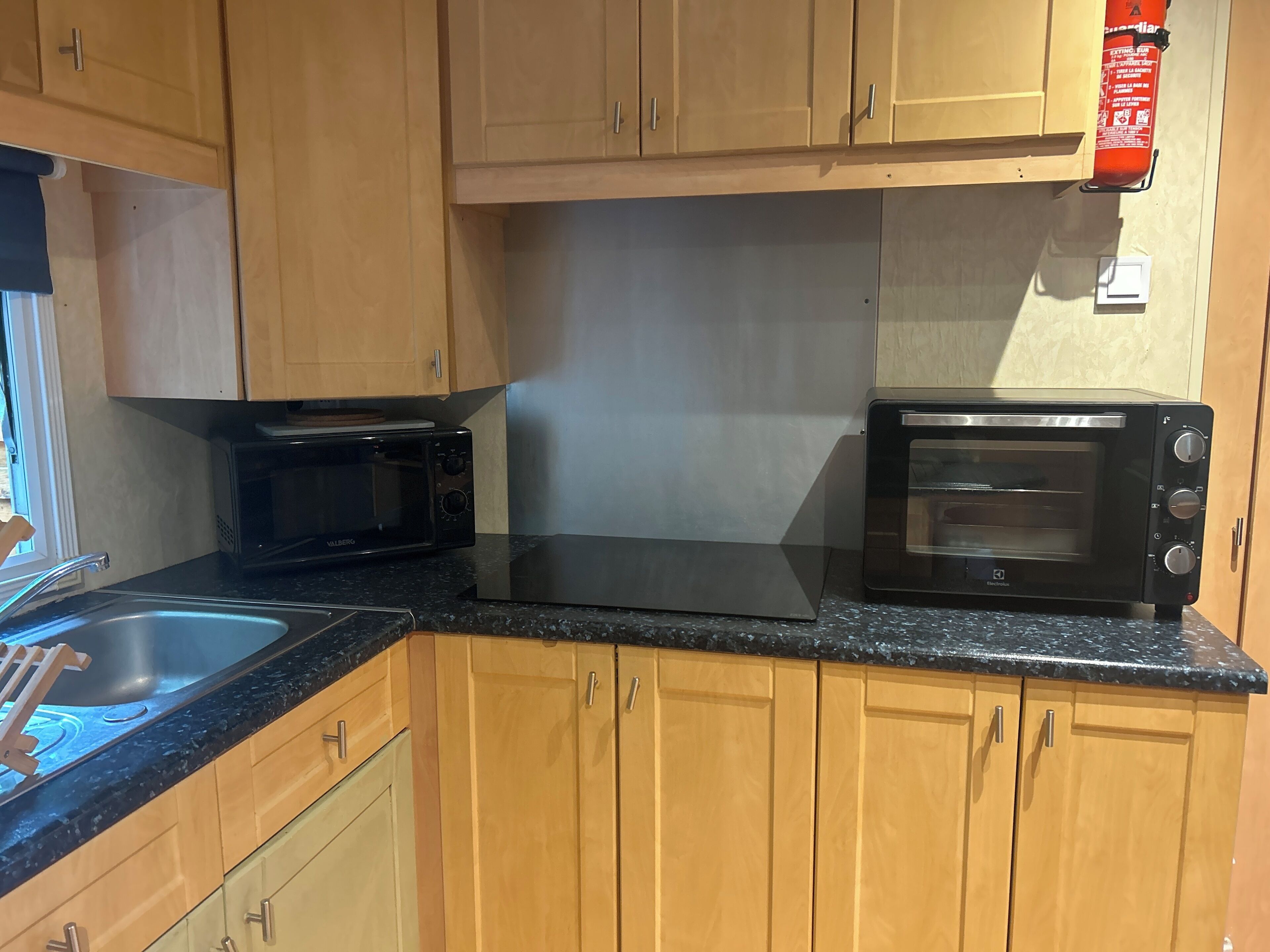A kitchen with wooden cabinets, a black countertop, a microwave, and a toaster oven.