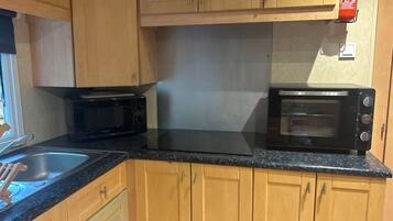 A kitchen with wooden cabinets, a black countertop, a microwave, and a toaster oven.