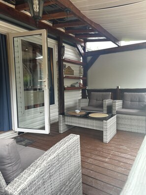 A covered outdoor seating area with wicker furniture and a glass door leading to a patio.