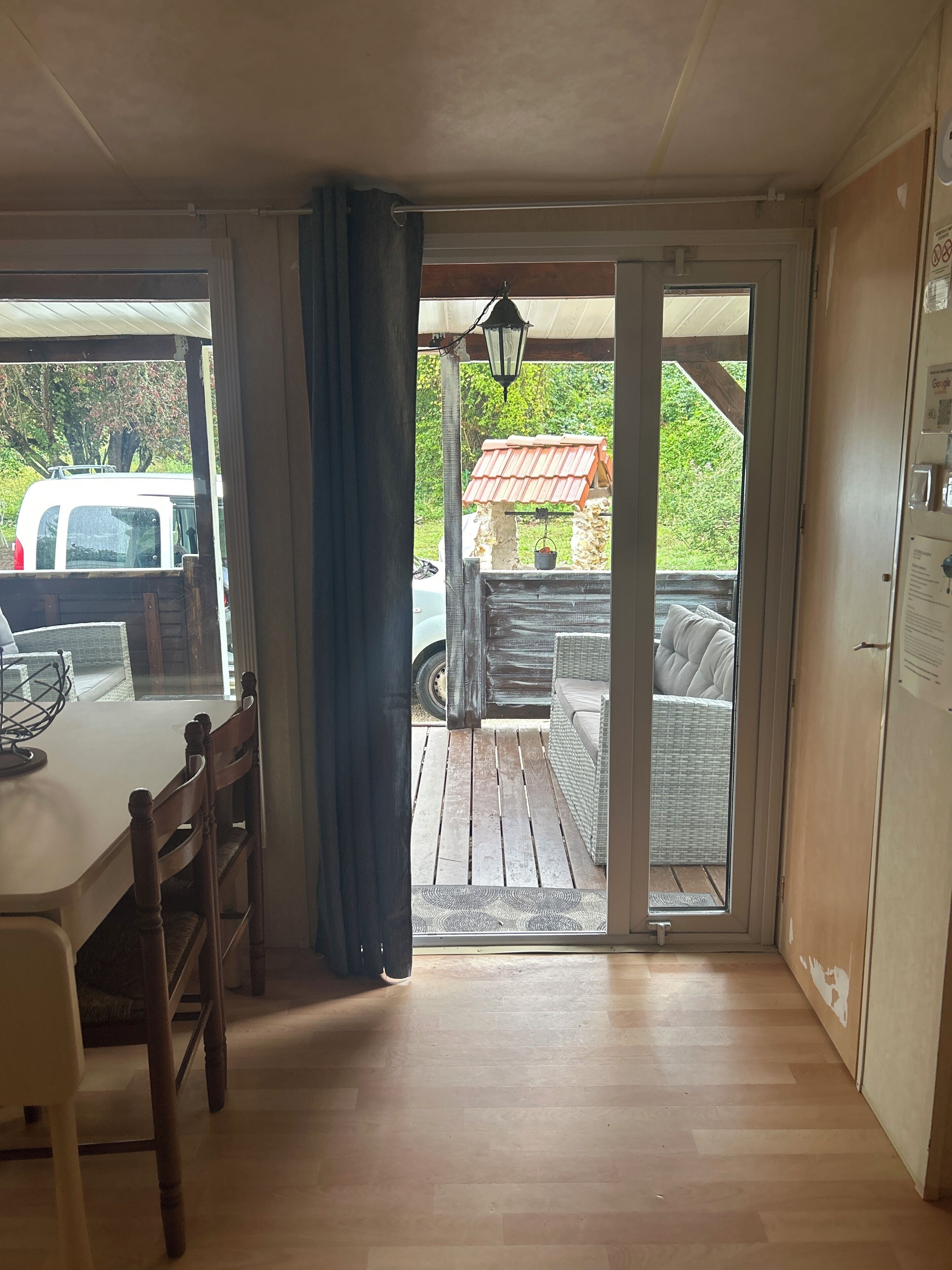 A room with a wooden table and chairs, a sliding glass door leading to an outdoor patio with a wicker sofa and a red-roofed structure.