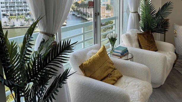 A modern living room with white plush sofas, a large window with sheer curtains, a view of a cityscape, and a potted plant. - Classy, Eclectic, Congenial hotel suite in charming Fort Lauderdale Florida (Fort Lauderdale)