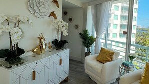 A modern living room with a white sofa, a white cabinet with geometric patterns, and decorative wall art including birds and flowers. - Classy, Eclectic, Congenial hotel suite in charming Fort Lauderdale Florida (Fort Lauderdale)