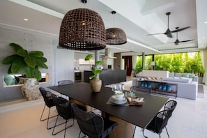 A modern dining area with a large table, chairs, hanging wicker lamps, and potted plants. - Muscat 3-Bedroom Villa with Beach Access (Koh Samui)