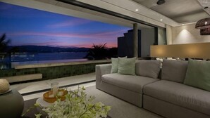 Ein modernes Wohnzimmer mit einer Couch, einem Couchtisch mit Blumenvase und Blick auf ein Gewässer im Abenddämmerung.