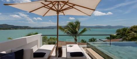 A balcony with a view of the sea, a pool, and lounge chairs.