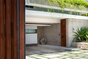 A modern building entrance with a concrete wall, a wooden door, and a stone planter. - Muscat 3-Bedroom Villa with Beach Access (Koh Samui)