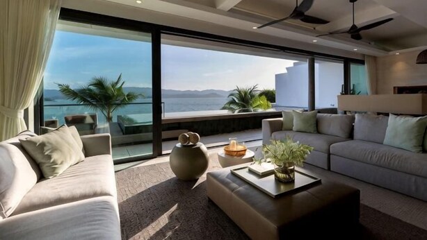 Ein modernes Wohnzimmer mit großem Fenster, einer Couch, einem Couchtisch und Deckenventilatoren.