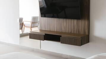 Quarto moderno com uma cama grande, televisão montada e um espaço de estar com cadeiras.