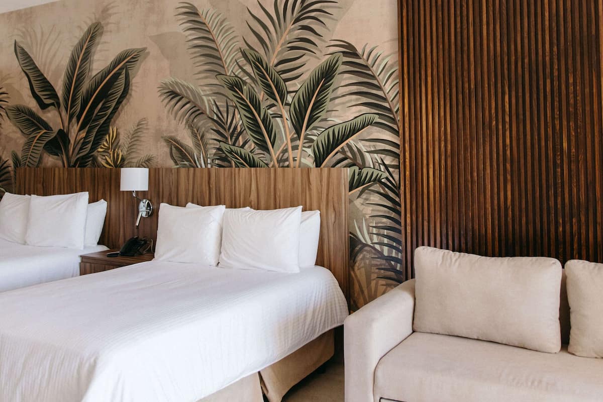 Habitación de hotel con una cama grande, un sofá y un mural de hojas tropicales.