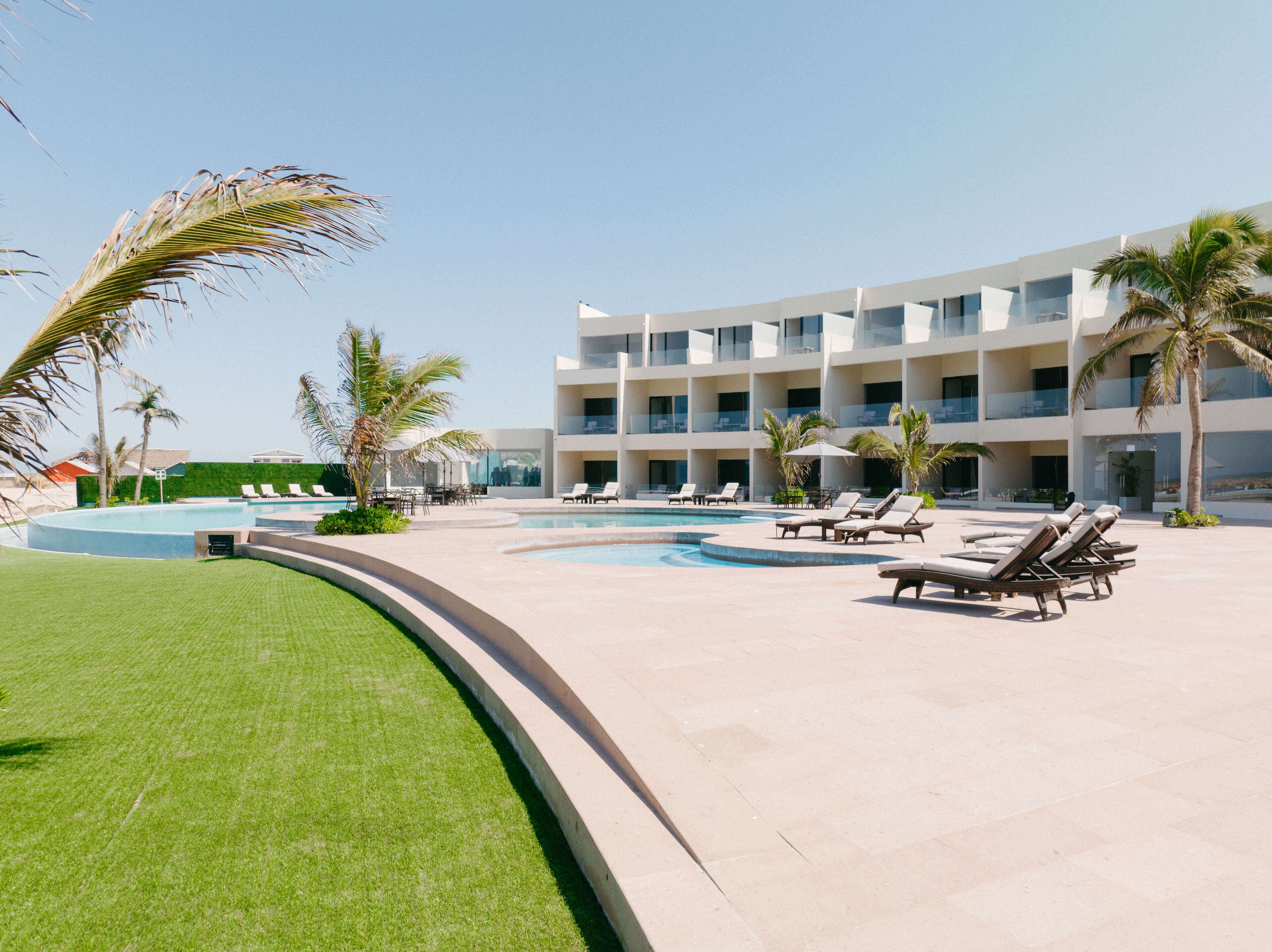 Un resort con piscina, sillas de descanso, palmeras y un edificio de varios pisos.
