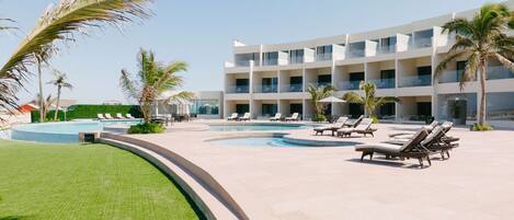 Un resort con piscina, sillas de descanso, palmeras y un edificio de varios pisos.