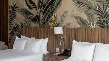 A hotel room with two beds, a wooden headboard, a nightstand with a lamp, and a wall mural of tropical leaves.