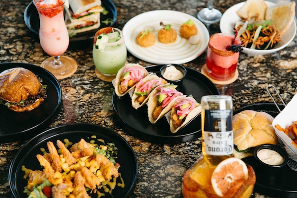 A variety of dishes including tacos, a burger, and shrimp, along with several drinks on a table.