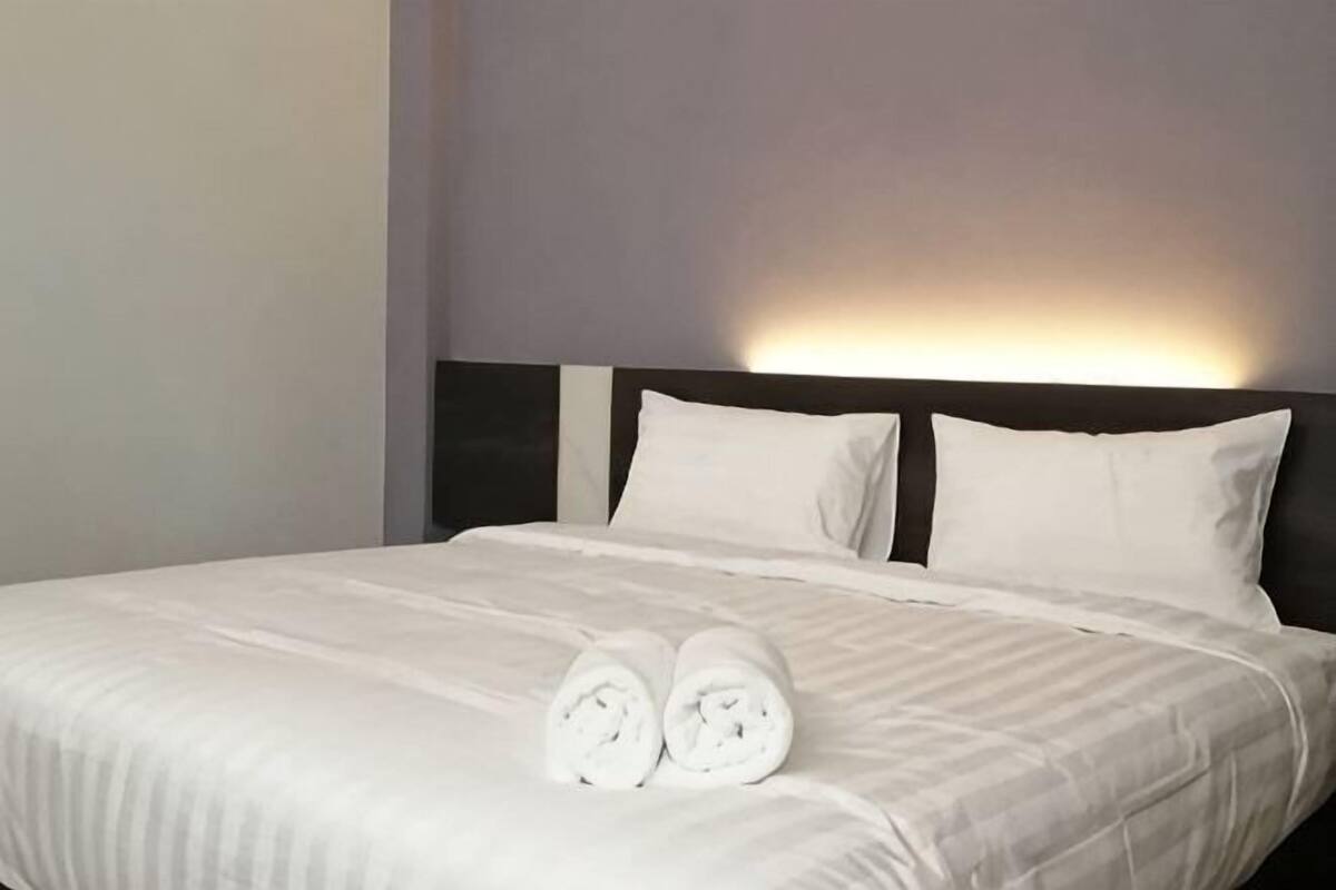 A neatly made bed with white linens and two rolled towels placed on the bed.