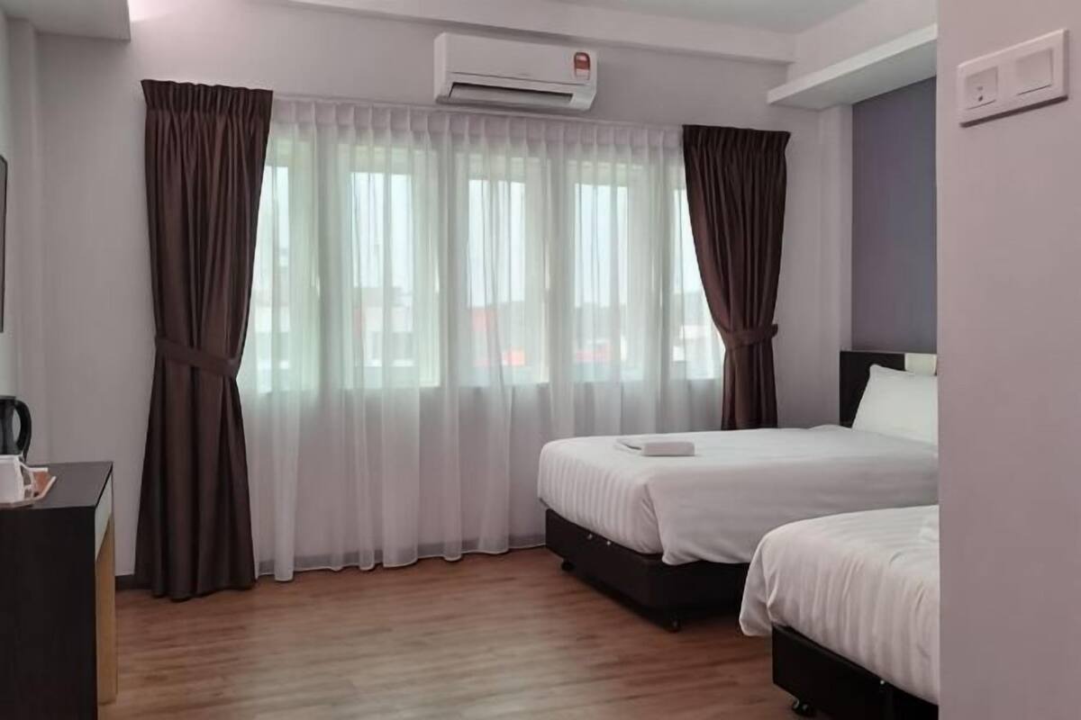A hotel room with two beds, a desk, an air conditioner, and a window with curtains.
