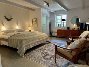 A bedroom with a bed, bedside lamps, a wooden dresser, a chair, and a window with a view of greenery.