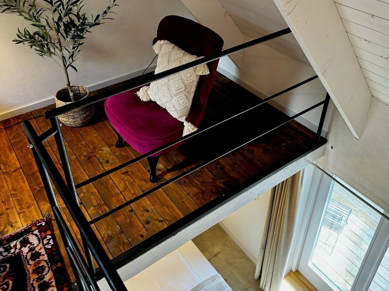 A high ceiling with a wooden floor, a red chair with a white throw, and a potted plant.