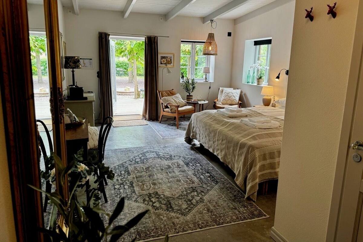 Ein Schlafzimmer mit einem Bett, einem Sessel, einem Schreibtisch, einer Lampe und einem Fenster.