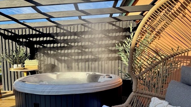 Ein Whirlpool in einer Gartenanlage mit Holzboden, Korbmöbeln und einer Pergola.