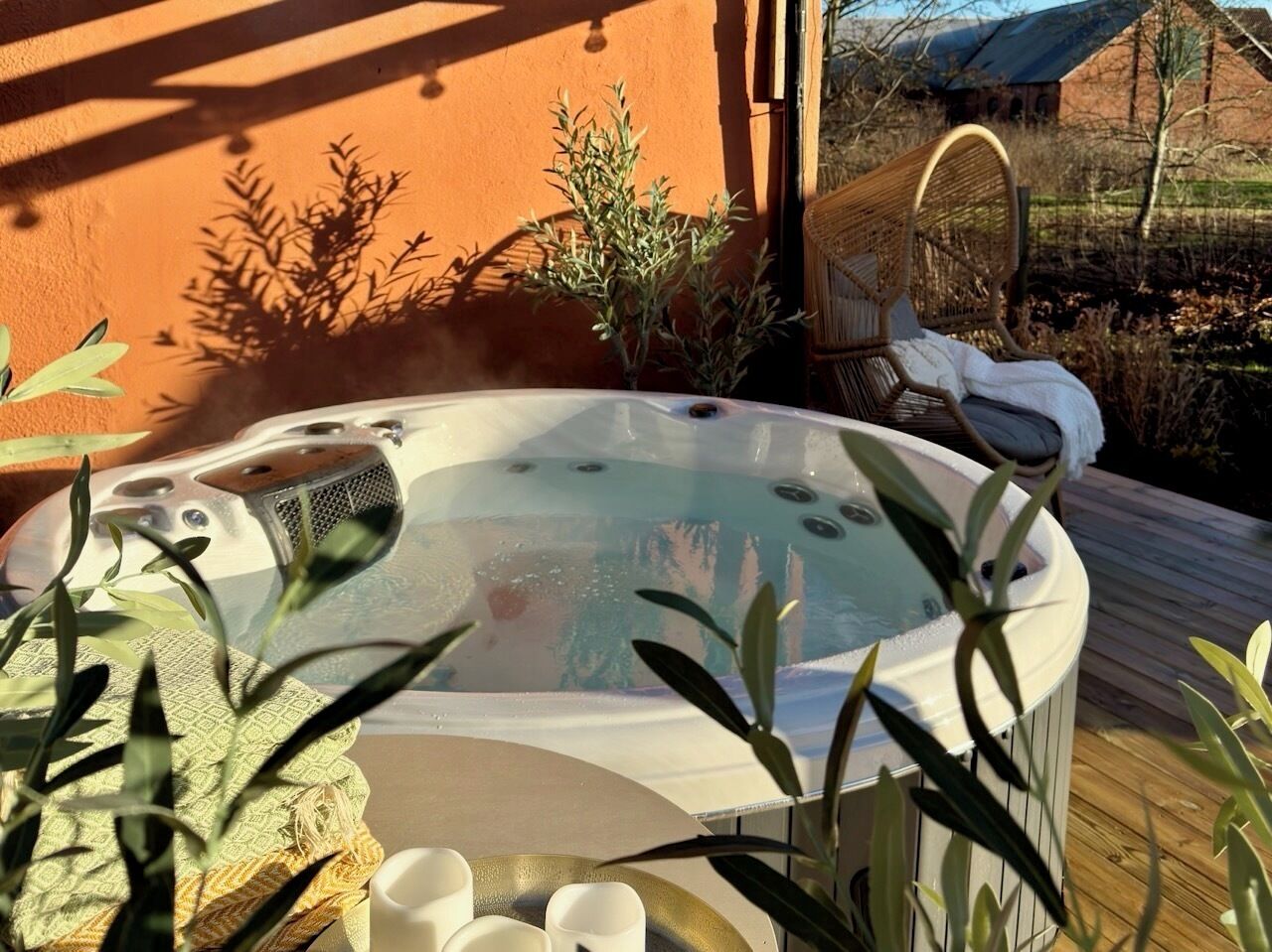 Un jacuzzi con tapa de vidrio transparente, rodeado de plantas y una terraza de madera.