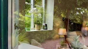 Blick durch ein Fenster auf eine Ablage mit Dekoration, eine Lampe und ein Glas.