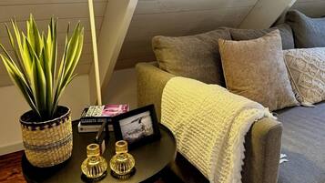 A cozy room with a grey sofa, a white throw blanket, and a small round table with a potted plant, a framed photo, and decorative vases.