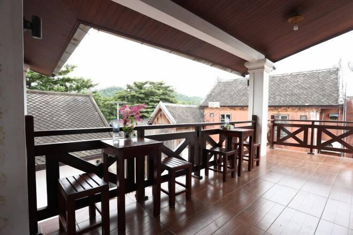 A covered outdoor area with wooden furniture and a view of buildings in the background.