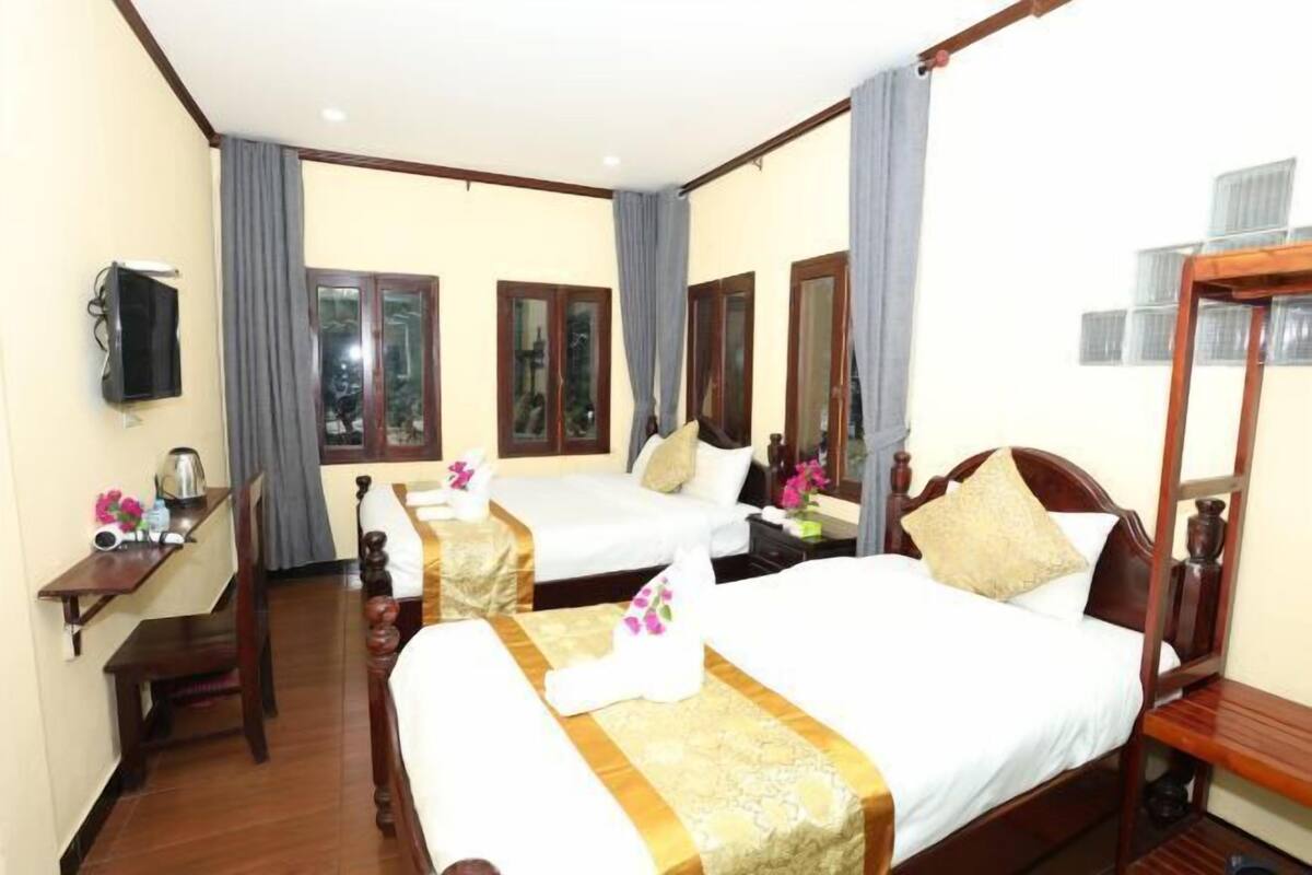 A hotel room with two beds, a desk, a TV, and a window with curtains.