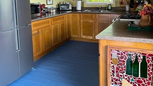 Una cocina con armarios de madera, un refrigerador de acero inoxidable, un microondas, un tostador y una ventana con persianas.