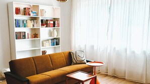 A living room with a sofa, a coffee table, a bookshelf, and a window with curtains. - NEW: Spacious suite with private terrace | 10 min from Rothenburg, ob der Tauber (Schrozberg)