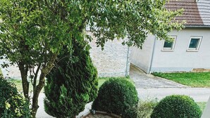 A wooden deck leading to a patio area with a stone floor, surrounded by greenery and a house in the background. - NEW: Spacious suite with private terrace | 10 min from Rothenburg, ob der Tauber (Schrozberg)