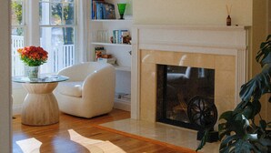 A living room with a fireplace, a white armchair, a glass coffee table with flowers, and a bookshelf. - Head of Pond House (Water Mill)