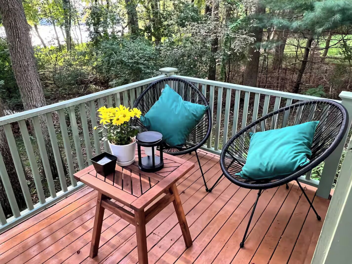 A wooden deck with two wicker chairs and a small table, surrounded by a white railing.