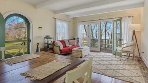 A cozy living room with a wooden table, a red sofa, and a balcony with a view of trees and a body of water. - Head of Pond House (Water Mill)