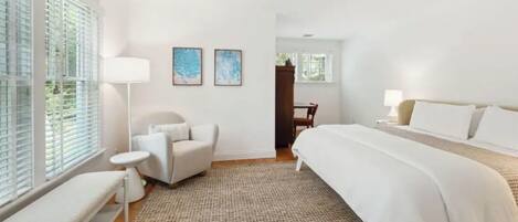 A hotel room with a large bed, a chair, a small table, and two artwork pieces on the wall.