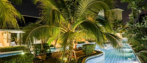 A swimming pool with a tiled edge, surrounded by palm trees and a lounge area.