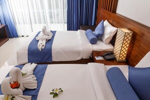 Une chambre d’hôtel avec deux lits, une tête de lit en bois, une table de chevet avec un téléphone et une boîte décorative, et une fenêtre avec des rideaux.