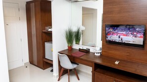 A hotel room with a wooden desk, a television mounted on the wall, a potted plant, and a white chair. - Tuana Hotels Brook Pool Access (Chalong)