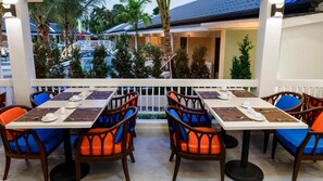 Un espace extérieur aménagé pour les repas, avec des tables et des chaises, donnant sur la rue, et avec un bâtiment visible au loin.