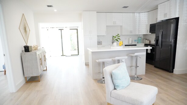 A modern kitchen with white cabinetry, a black refrigerator, and a bar area with stools.