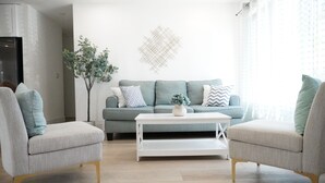 A modern living room with a grey sofa, two armchairs, a white coffee table, and a decorative plant.
