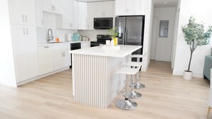 A modern kitchen with white cabinetry, a central island with bar stools, a stainless steel refrigerator, and a microwave above the stove.