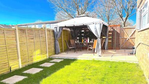 Un jardin avec un patio couvert, une clôture en bois et une pelouse.