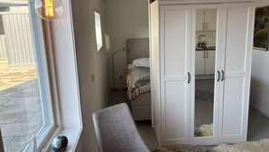 Un dormitorio con cama, armario, silla, lámpara y ventana con bombilla.