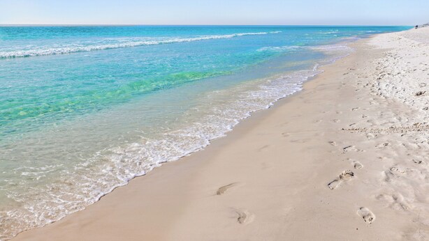 Une plage à l’eau turquoise et limpide, bordée d’un rivage sablonneux.