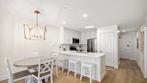 Une cuisine moderne avec des meubles blancs, un îlot central et un coin repas avec des chaises blanches.