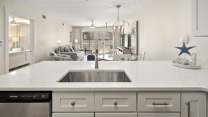 Une cuisine moderne équipée d’un lave-vaisselle, de meubles blancs et d’un grand îlot central doté d’un évier.