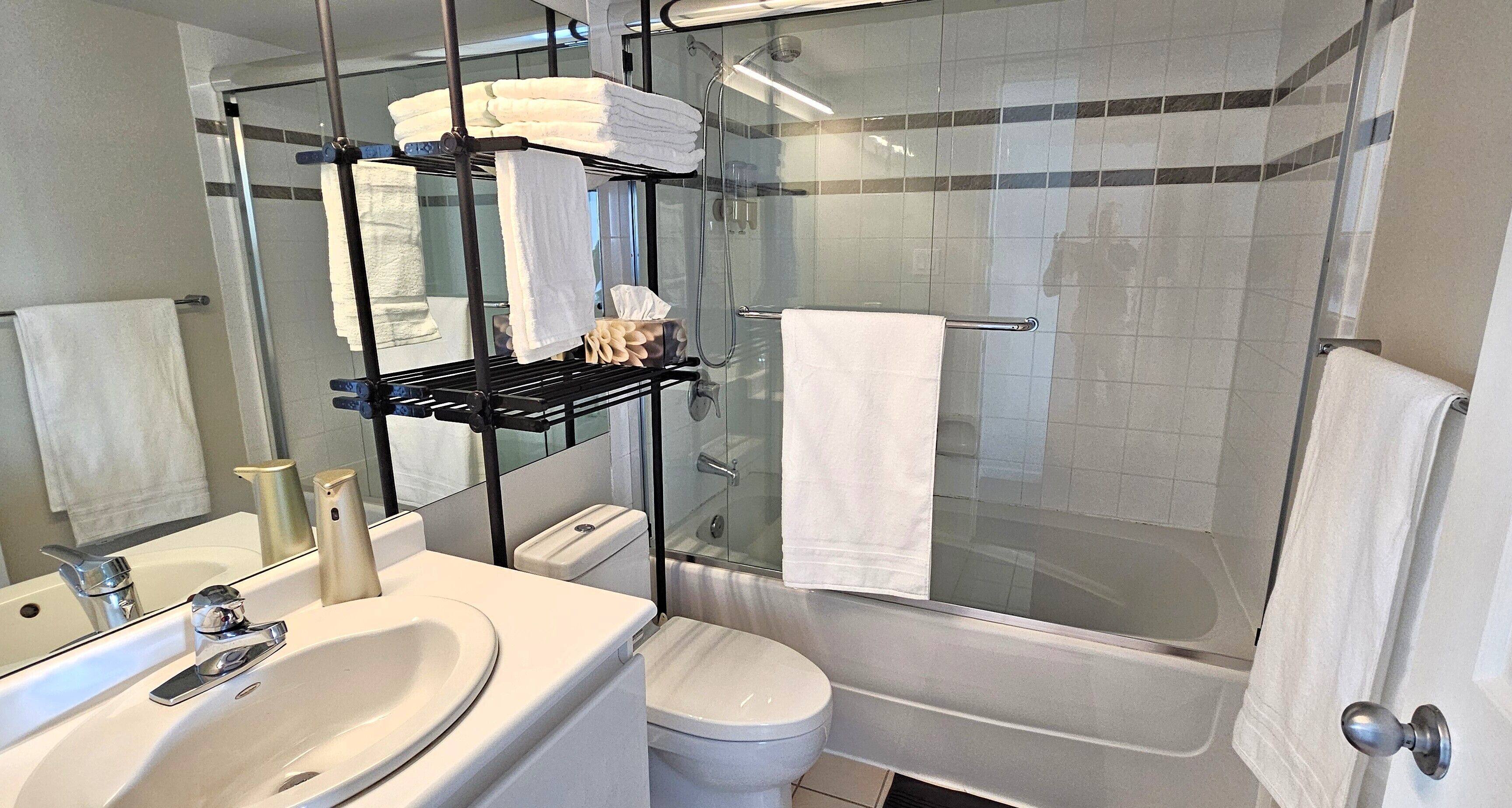 Ein modernes Badezimmer mit einer gläsernen Dusche, einem weißen Waschbecken und einem Handtuchhalter mit gefalteten Handtüchern.